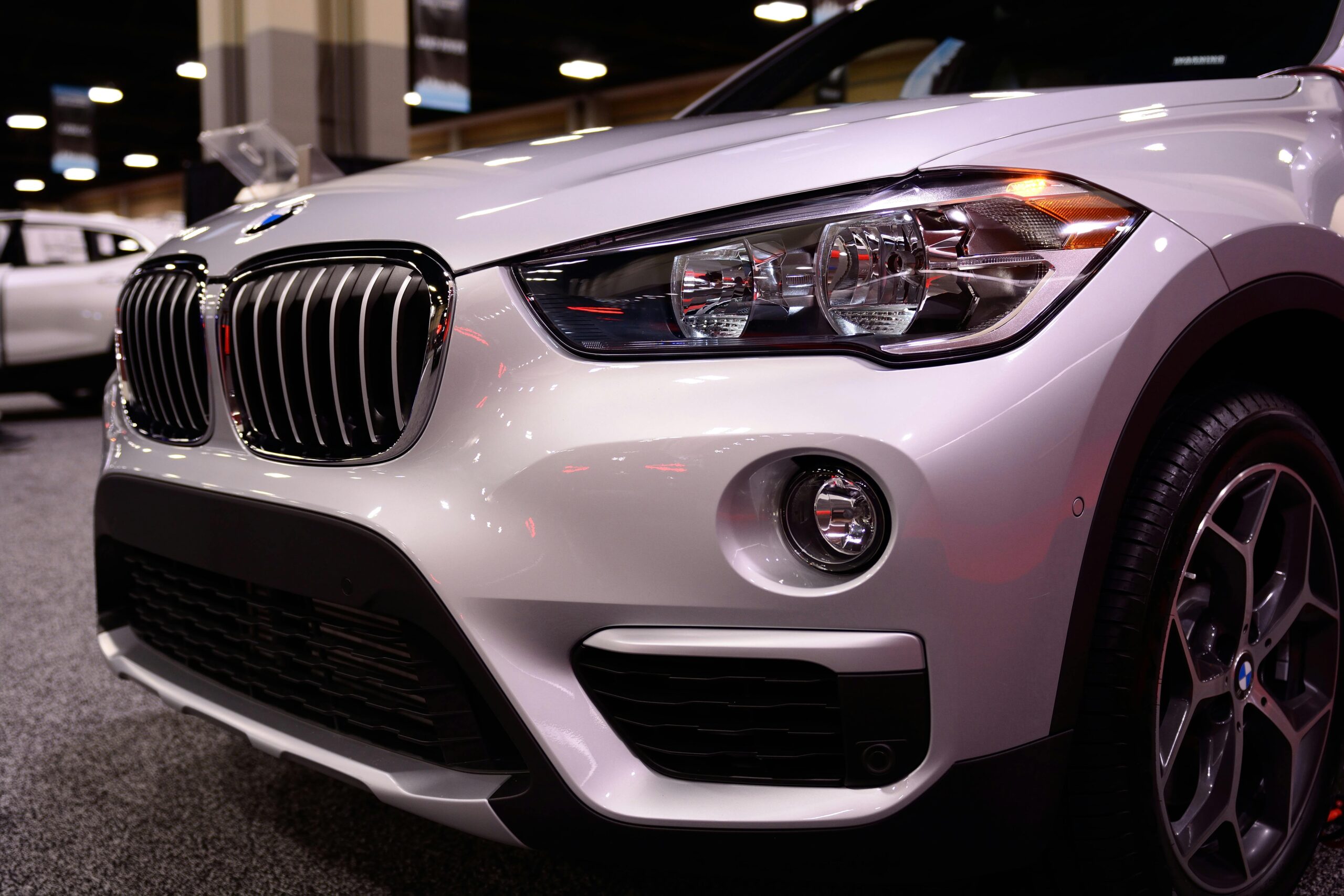Close-up of a luxury car's front end showcasing its sleek design at an indoor auto show.